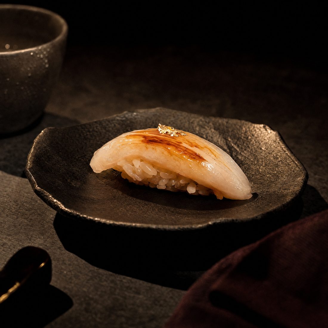 A single piece of nigiri, plated on dark ceramic